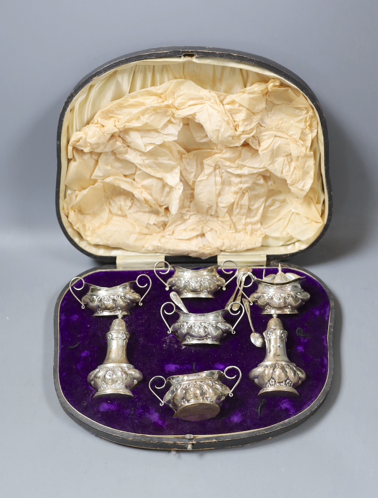 A late Victorian embossed silver six piece condiment set, together with four spoon, Sheffield, 1901, by Walker and Hall.